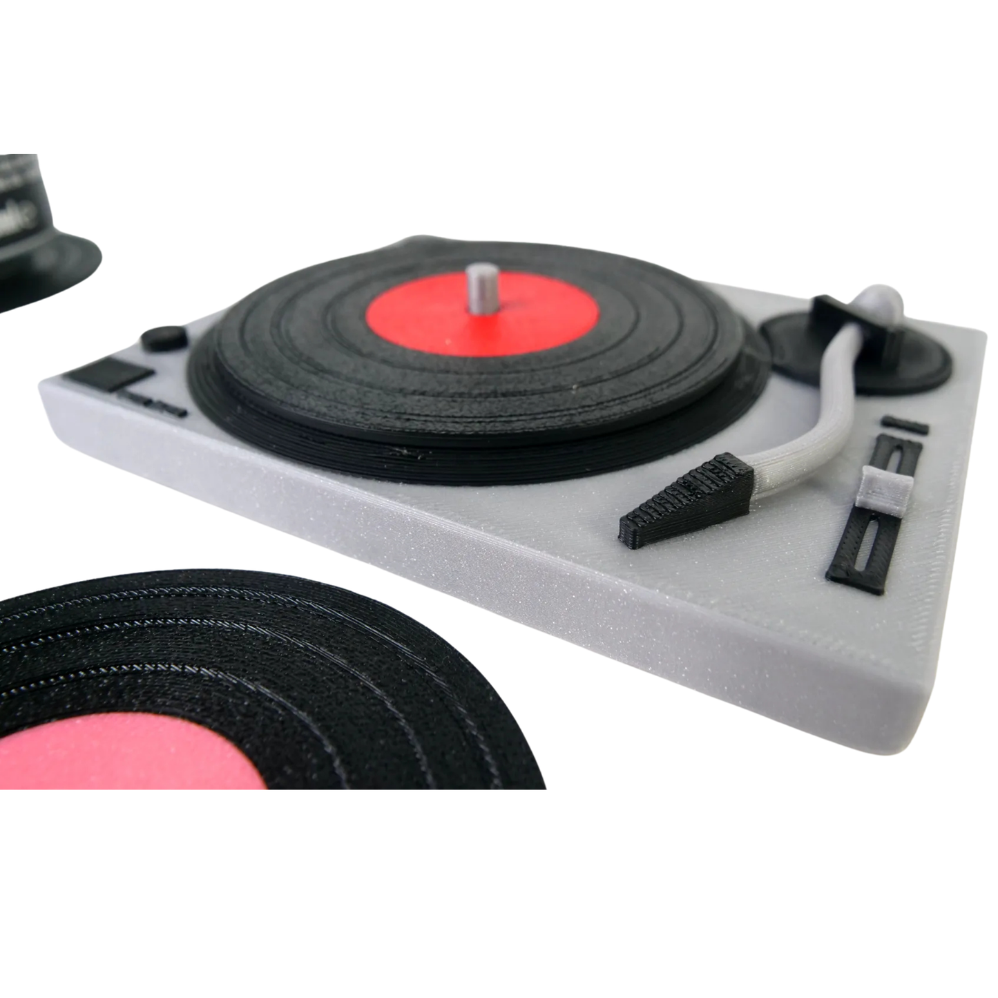 Primer plano de la miniatura de tocadiscos gris con un posavasos de disco de vinilo con etiqueta roja colocado sobre su plato, mostrando el brazo del tocadiscos.