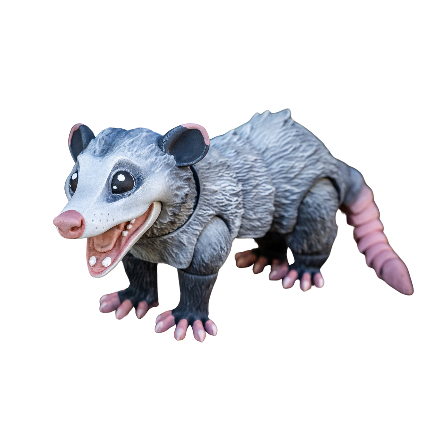 Figura articulada de zarigüeya en color gris, con boca abierta y una expresión que simula una sonrisa, posada de forma amigable.