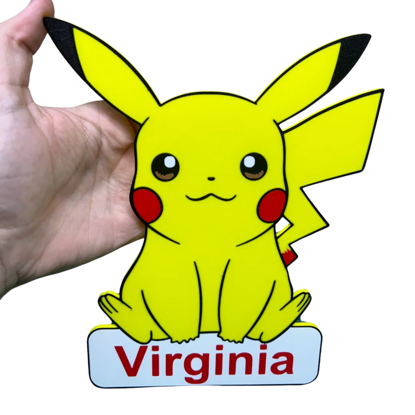 Figura decorativa de Pikachu Pokémon con el nombre "personalizado" en la base, mostrando el personaje amarillo con sus orejas negras y mejillas rojas, sostenido por una mano.