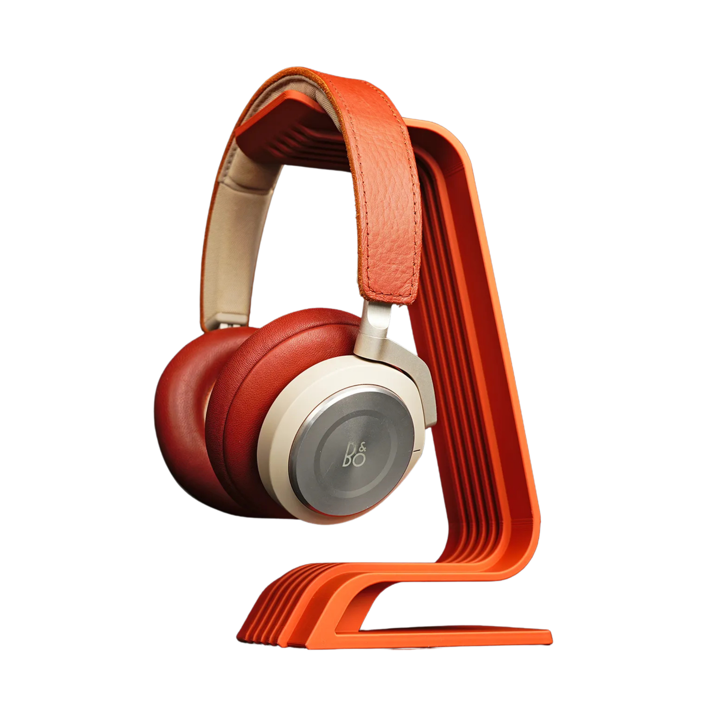 Porta audífonos de diseño minimalista curvo en color naranja, sosteniendo unos auriculares over-ear rojos y crema, visto de frente.
