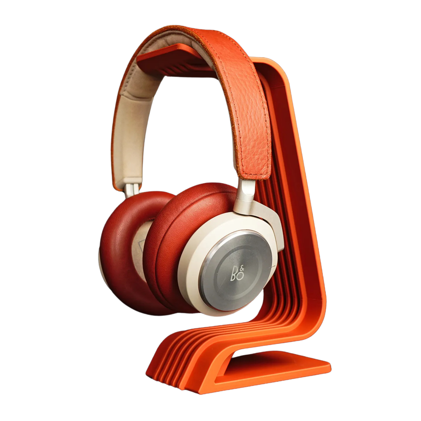 Soporte para audífonos de diseño curvo en color naranja, con auriculares rojos y crema colgados, mostrando el ángulo ergonómico de apoyo.