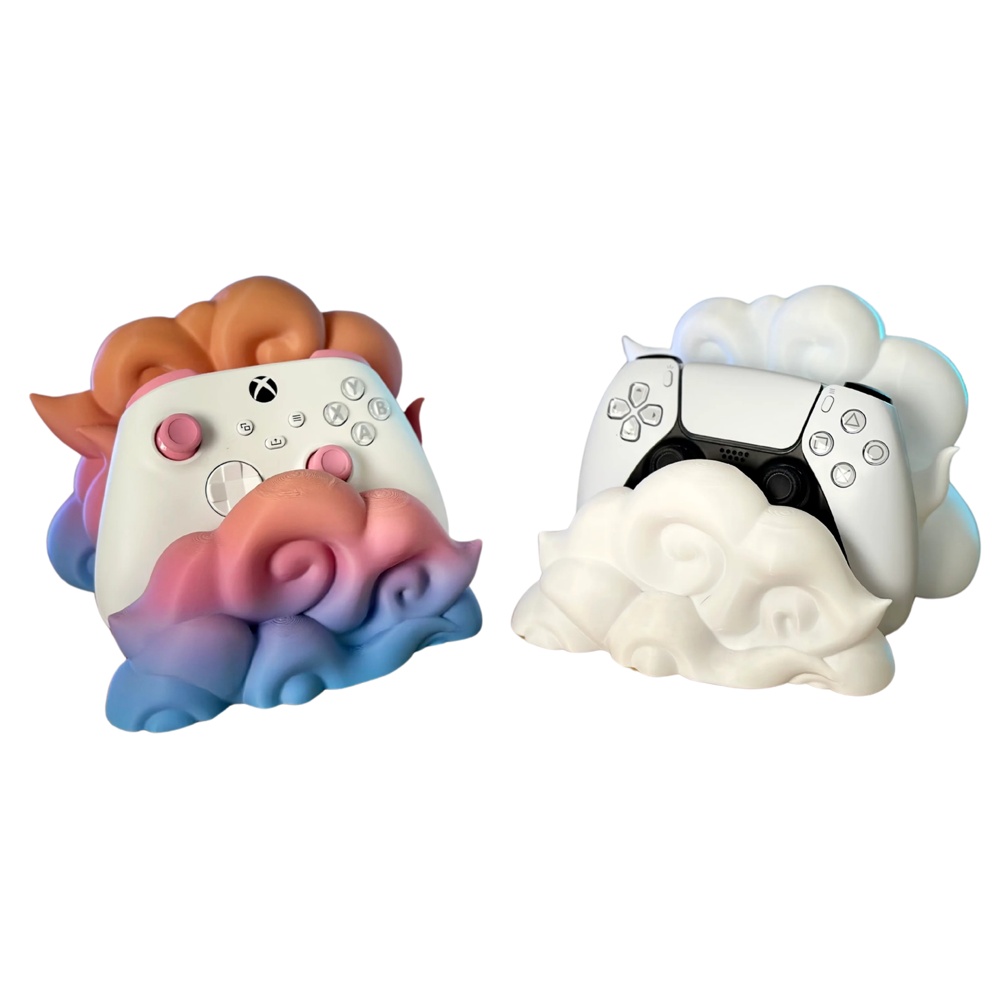 Soportes para mandos de consolas Xbox y PS5 en forma de nube, destacando el diseño degradado rosa y azul de un porta joystick y el blanco del otro.