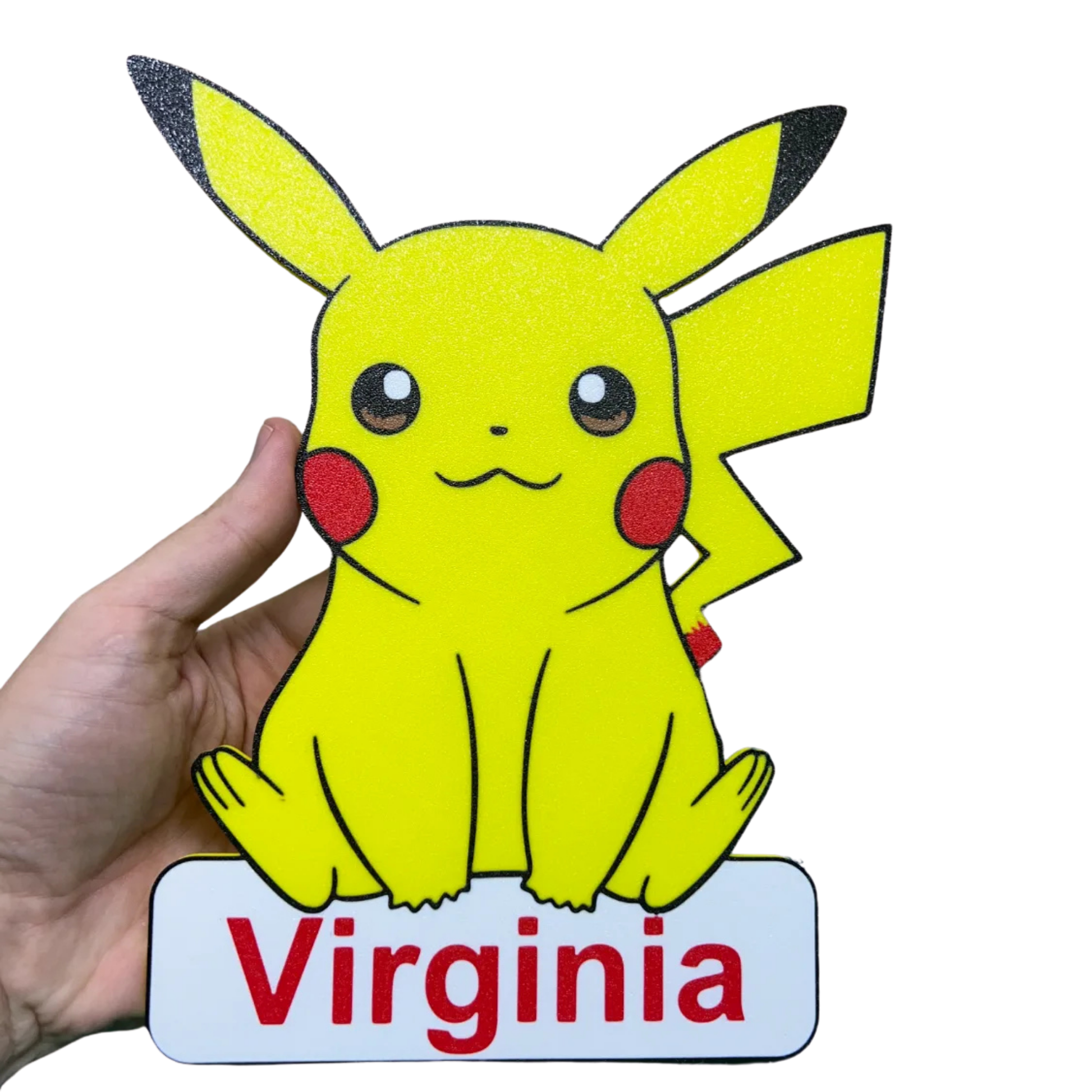 Aplique decorativo de Pikachu Pokémon en color amarillo, con mejillas rojas y cola de rayo, sobre una base con el nombre "personalizado", sostenido por una mano.