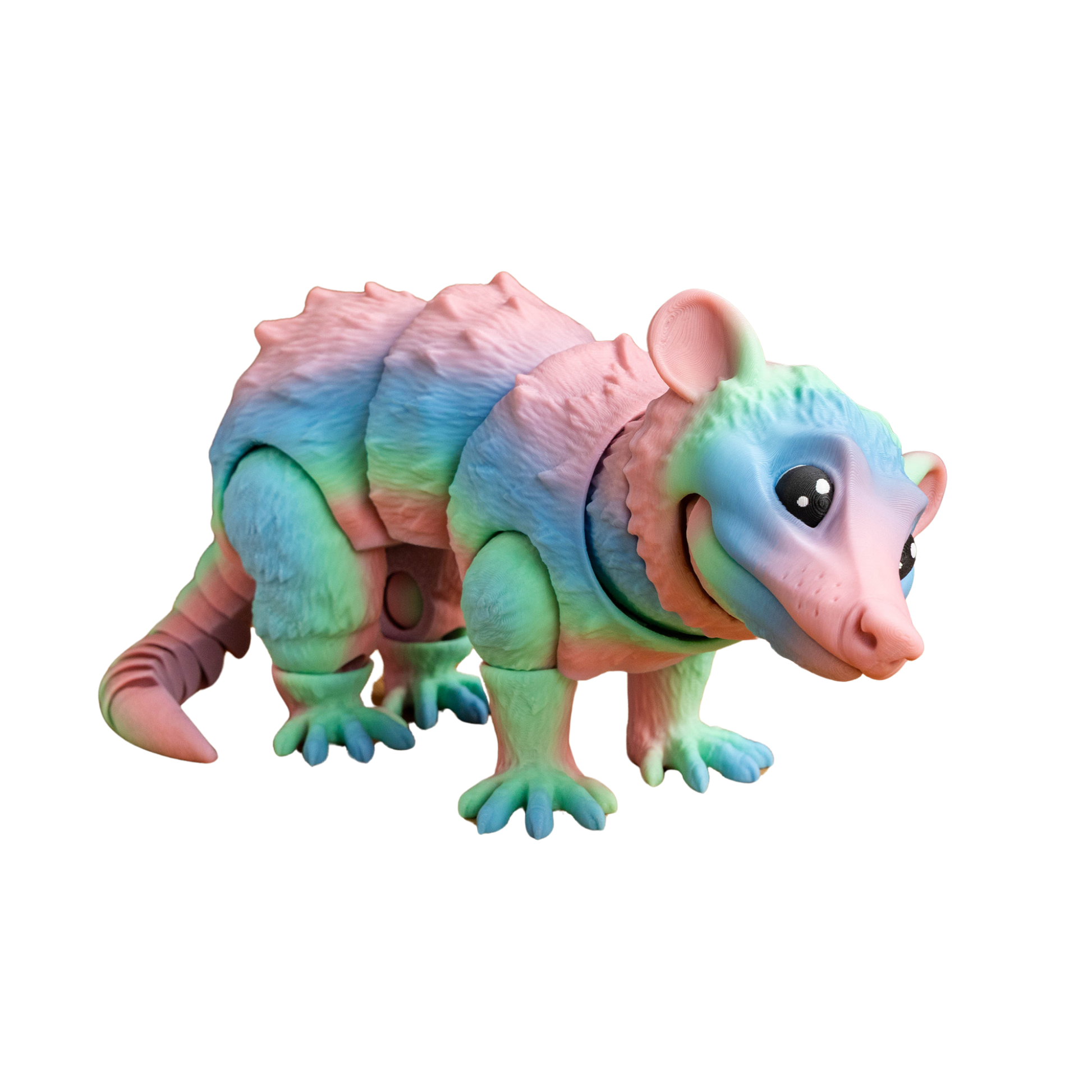 Figura articulada de zarigüeya en tonos pastel (rosa, azul, verde), con boca cerrada y expresión curiosa, posada sobre sus cuatro patas.