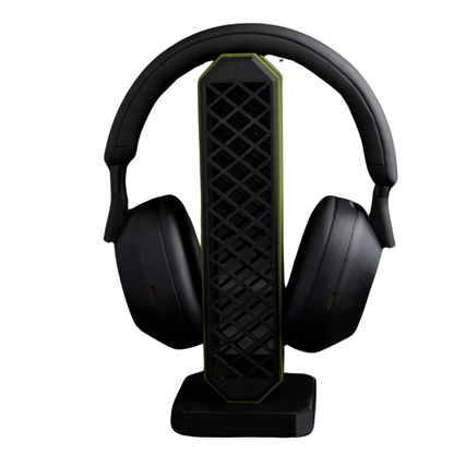Porta audífonos gaming vertical en color negro con detalles verdes y patrón de rejilla, sosteniendo unos auriculares gaming negros.
