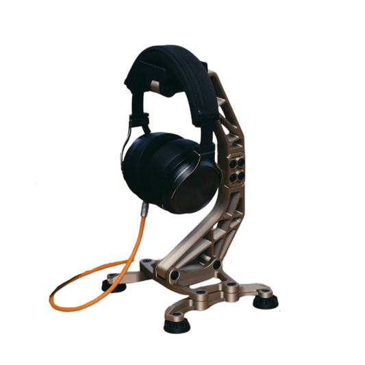 Porta audífonos de diseño industrial con acabado metálico (bronce/champagne), sosteniendo unos auriculares negros con un cable naranja, sobre una base estable.