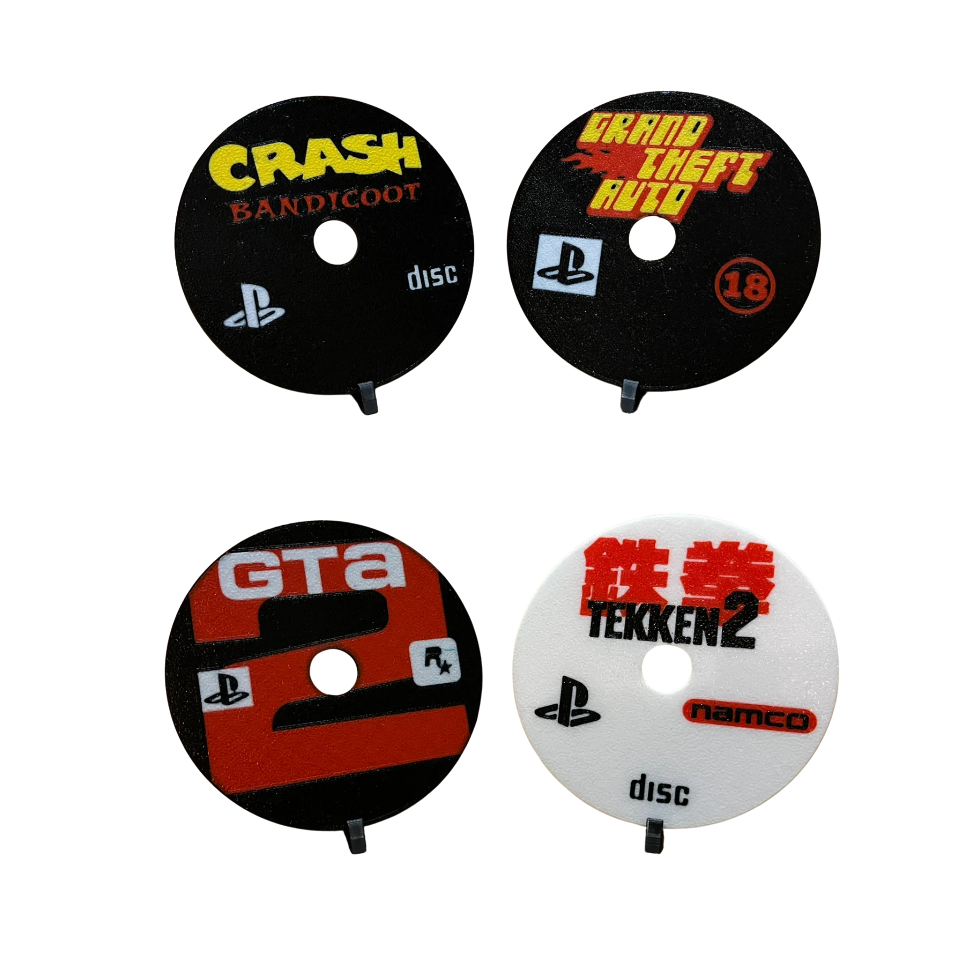 Cuatro posavasos de discos de PlayStation 1: Crash Bandicoot (negro), Grand Theft Auto (negro), GTA 2 (negro y rojo) y Tekken 2 (blanco y rojo).