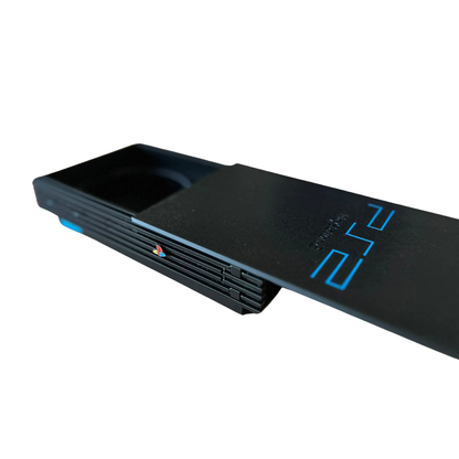 Vista lateral de la réplica de la consola PlayStation 2 Slim negra, con la bandeja de los posavasos ligeramente abierta, mostrando el mecanismo deslizable.