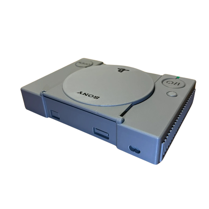 Réplica en miniatura de la consola PlayStation 1 gris, vista lateral de frente, mostrando la ranura para Memory Card y los detalles del diseño.