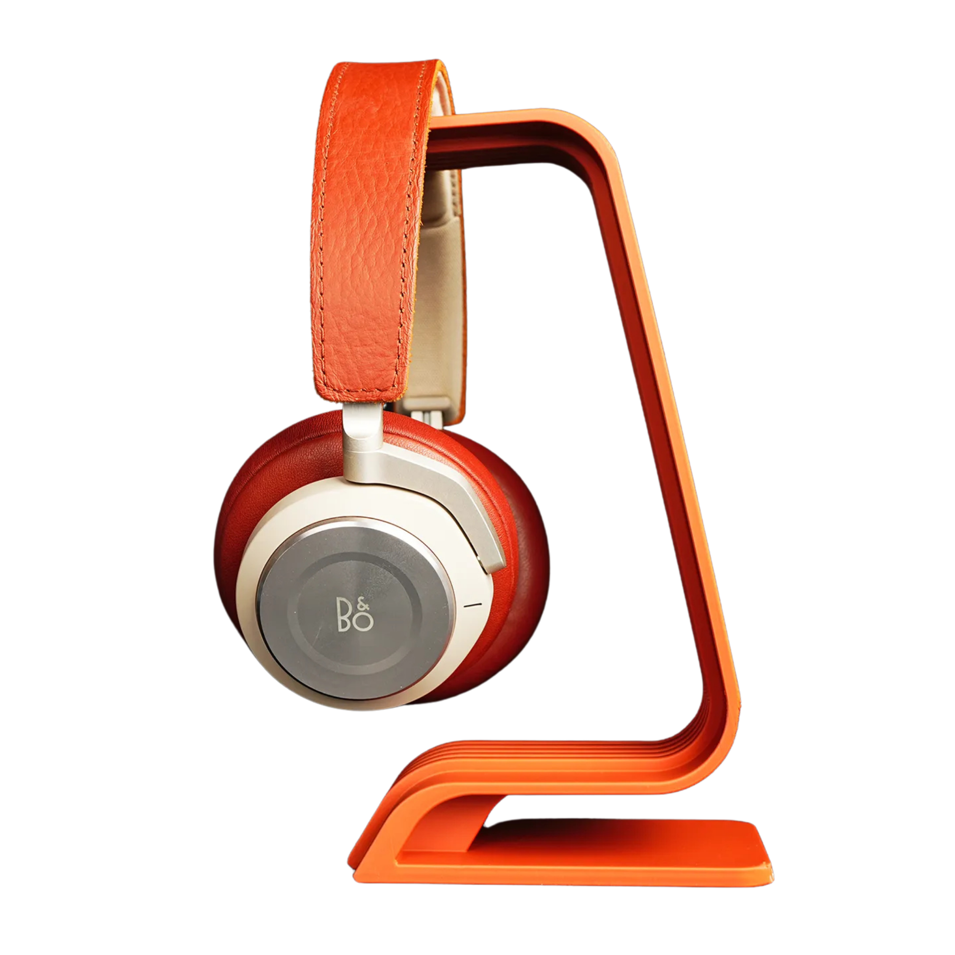 Soporte para audífonos de diseño curvo y estriado en color naranja, sosteniendo unos auriculares over-ear de color rojo y crema, visto de lado.