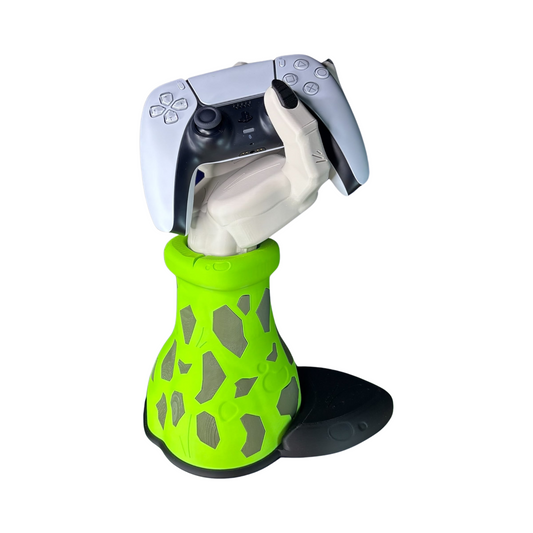 Soporte de mando gaming con diseño de la mano de Cell de Dragon Ball Z, sosteniendo un control de PS5 blanco, sobre una base verde con patrones.