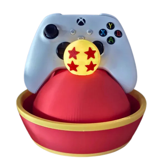 Soporte de mando gaming con diseño del sombrero de Gohan (Dragon Ball Z) rojo y amarillo, con una Esfera del Dragón de 4 estrellas amarilla, sosteniendo un control de Xbox blanco.