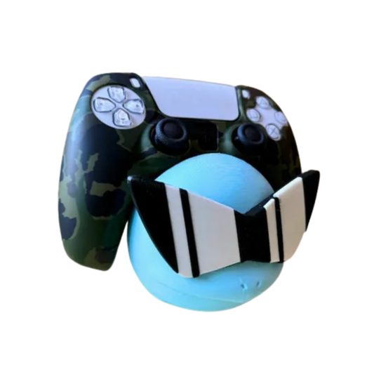 Soporte de mando gaming con diseño de la cabeza de Squirtle (Pokémon) en azul con gafas de sol pixeladas, sosteniendo un control de PS5 camuflado.
