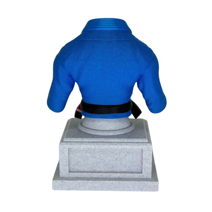 Vista trasera del trofeo de Gi de Jiu-Jitsu azul con cinturón negro y base gris, mostrando la textura del Gi.